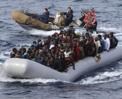 Migrants Sit In A Boat During A Rescue Operation By Italian Navy Off The Coast Of The South Of The Italian Island Of Sicily